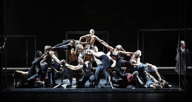 Group of people entwined in a pile, layering and climbing on each other like a low pyramid.