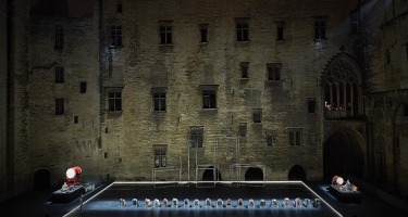 Wide shot of stage with a row of people on their hands and knees facing forward, with a taiko drum on either side.