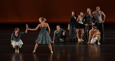 Two women do swing-type dance together while group watches.