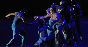 Man reaches towards another on the left while being restrained by group of dancers