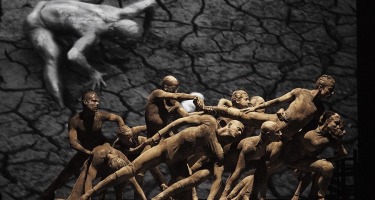 Group of mud covered dancers lurch in unison to the right.