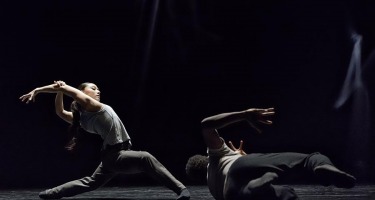 Dancer on left lunges with arms raised, dancer on right rolls on ground.