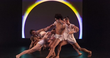 Group of dancers with backlit circle projected behind them.