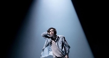 Man in spotlight with hand to ear as if listening.