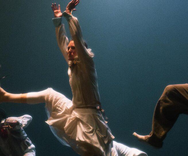 Hofesh Shechter Company. Three men leap with arms raised and one foot in the air.