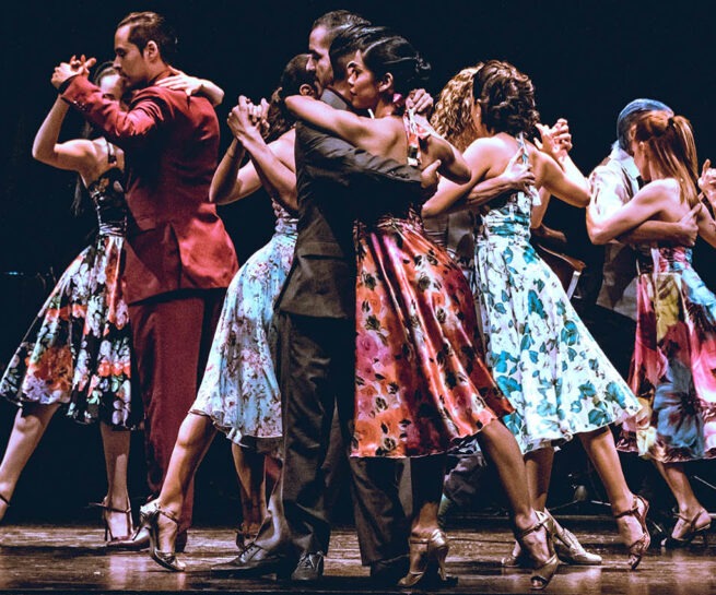 People in suits and floral dresses dance tango.